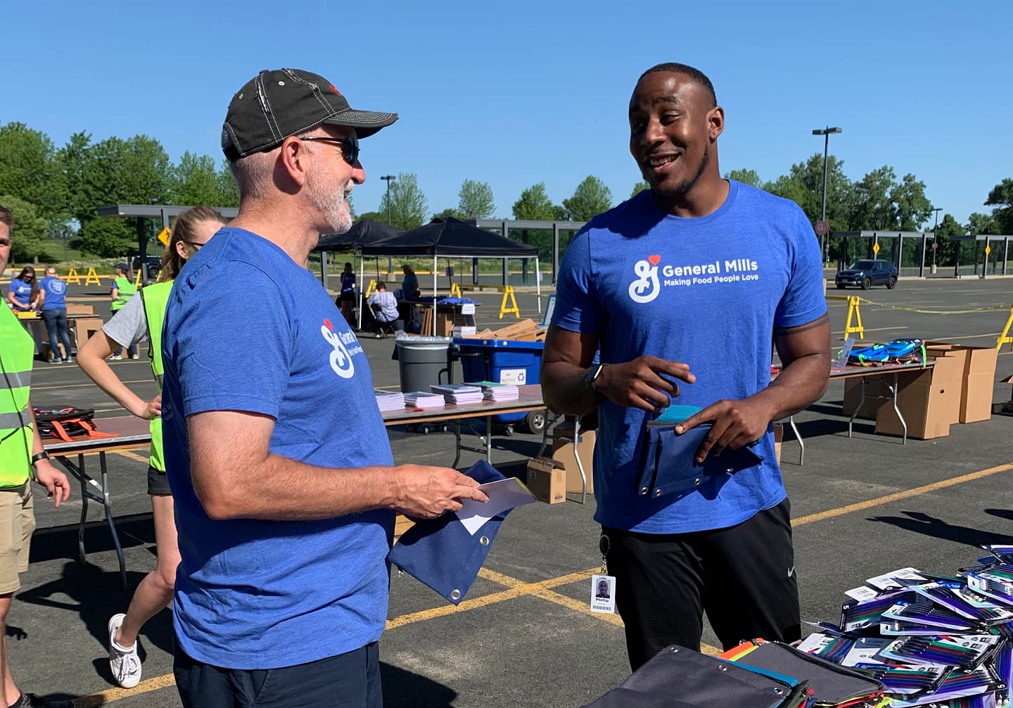 Two men in blue shirts having General Mills Logo printed on it engaged in conversation at a table, sharing ideas and insights in a collaborative setting.