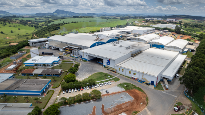 Aerial view of a large industrial complex with multiple white-roofed buildings surrounded by greenery and parking lots.
