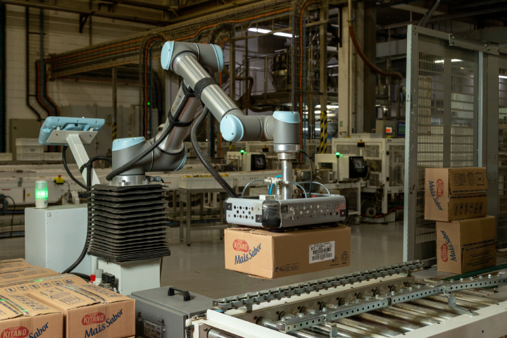A robotic arm arranges cardboard boxes on a conveyor belt in an industrial setting.