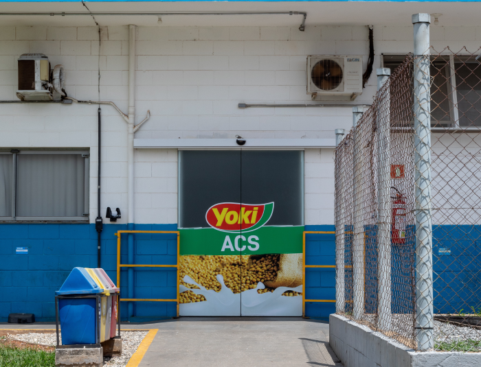 Entrance to a building with a Yoki ACS sign on the doors, flanked by a fence and waste bins on the left.