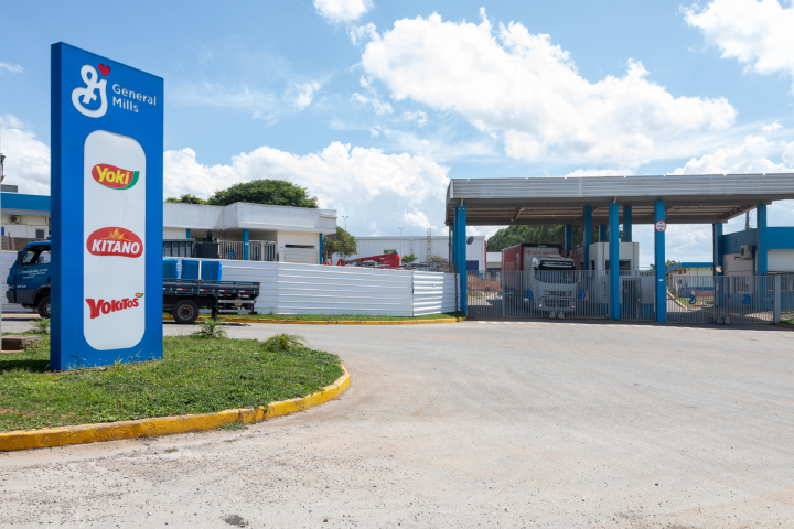 Entrance to a General Mills facility featuring a branded sign with logos for Yoki, Kitano, and Yokitos beside a gated entry, truck visible inside.