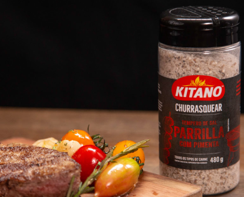 A juicy steak and fresh vegetables resting on a wooden cutting board next to a bottle of Kittano seasoning, ready to be grilled for a delicious meal.
